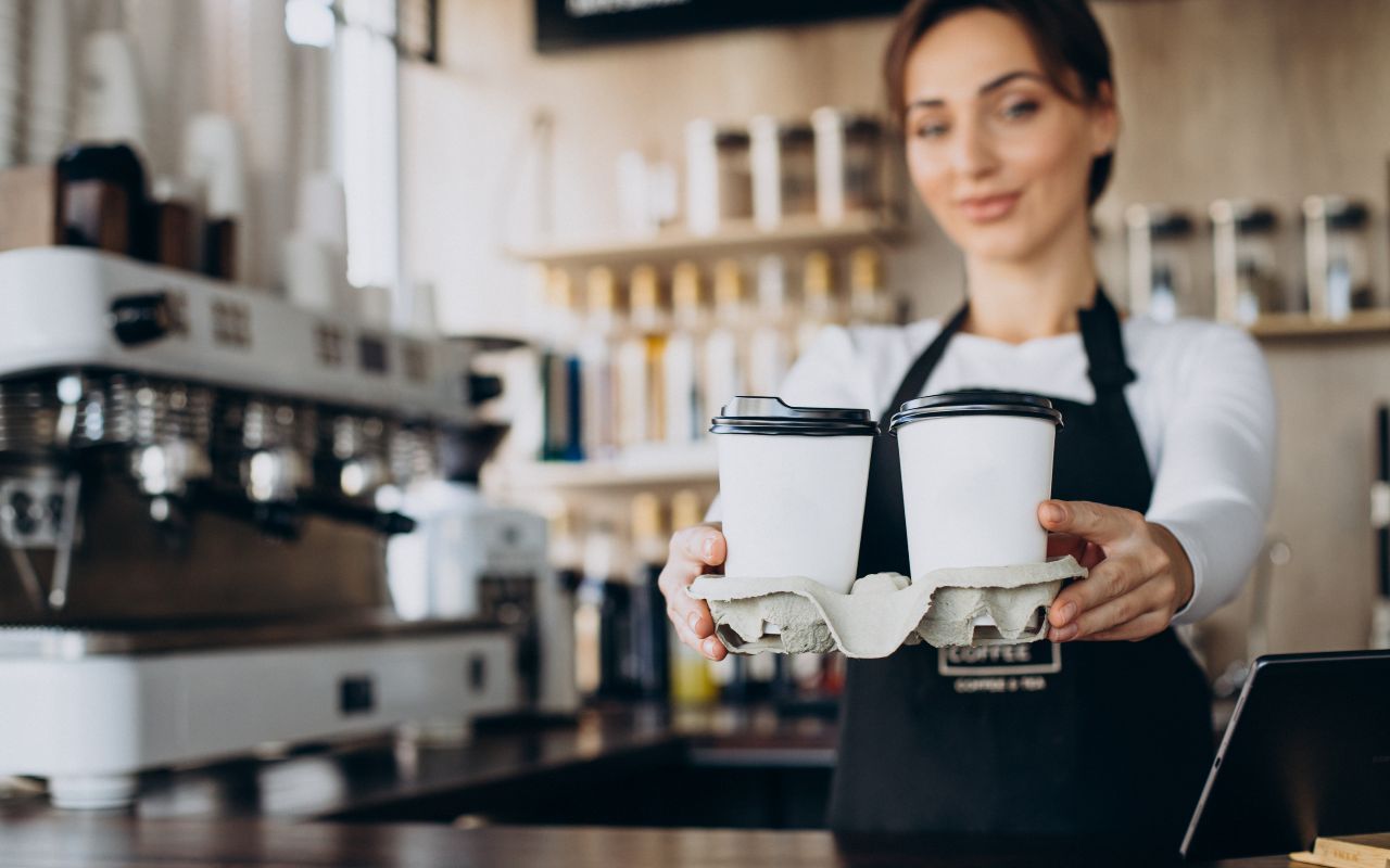 Una barista dietro il bancone porge due caffè a portare via