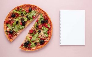 Pizza tagliata con olive e verdure vicino a un blocco da compilare per la dieta