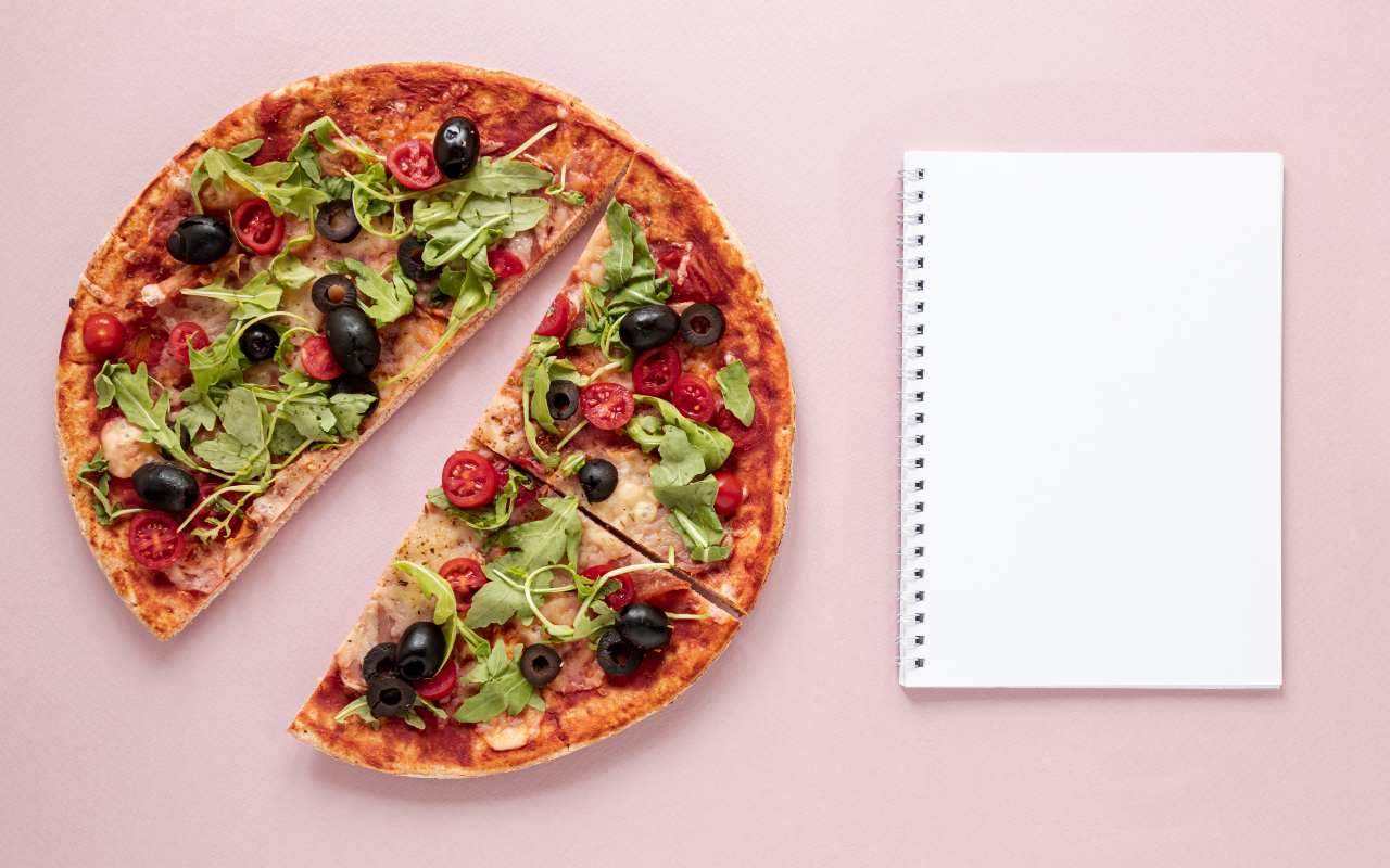 Pizza tagliata con olive e verdure vicino a un blocco da compilare per la dieta