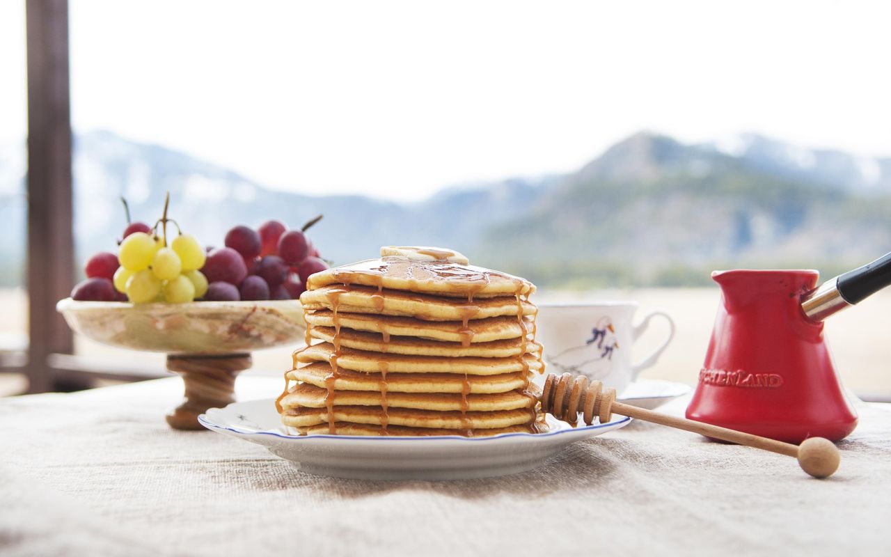 Un piatto di pancake su un tavolo vicino a un vassoio con uva e un bricchetto per il caffè