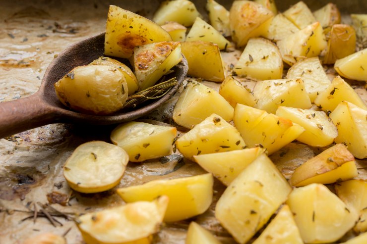 Patate al forno su una teglia con un cucchiaio di legno