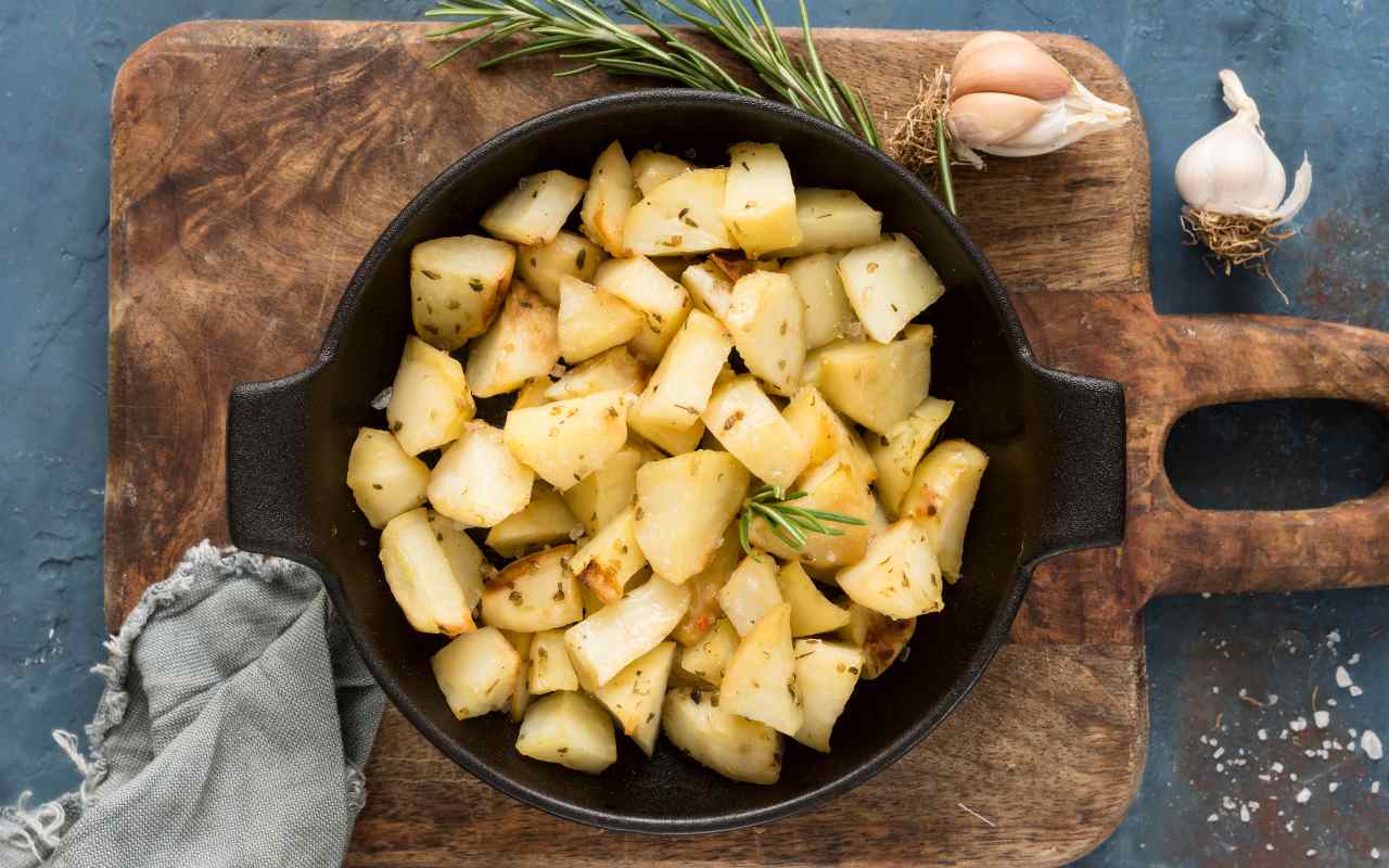 Patate in teglia su un tagliere di legno accanto a degli spicchi di aglio