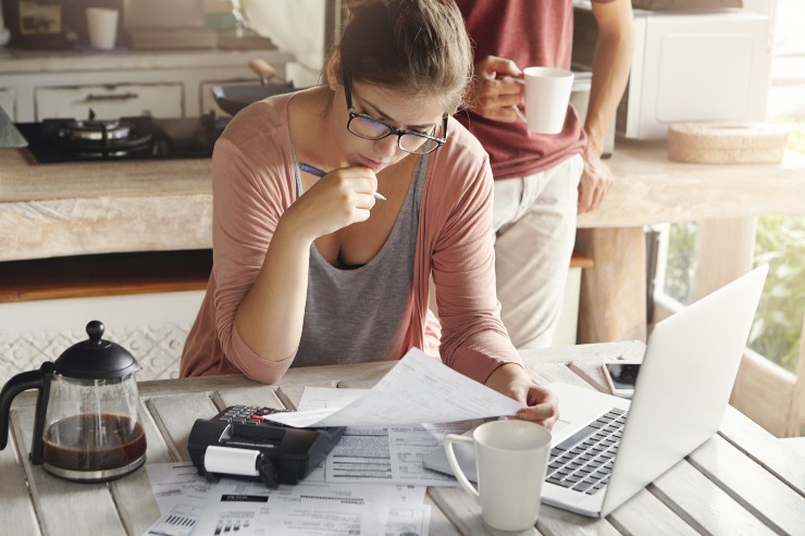 Una persona impegnata nei calcoli per le tasse con pc, documenti, calcolatrice e caffè su un tavolo